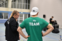 Ein Mann steht in einer Sportgalle und träft die Rückenaufschrift "TEAM".